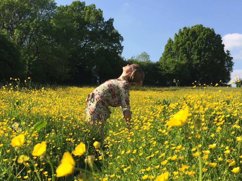 woman standing in a backbend yoga pose in a buttercup field