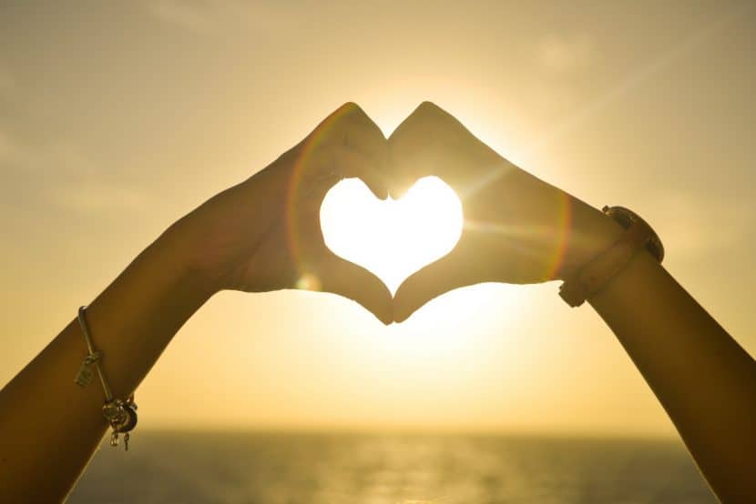 two hands making the shape of a heart in front of the setting sun