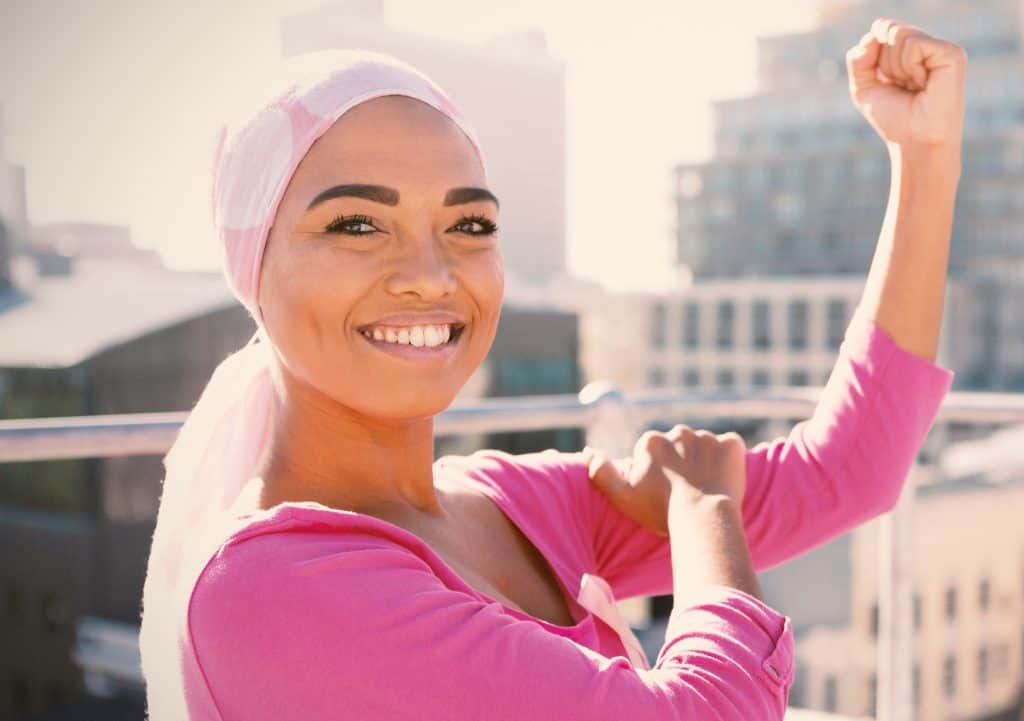 young woman with a scarf on her head that looks like a cancer patient holding her arm up in the air in a muscle pose