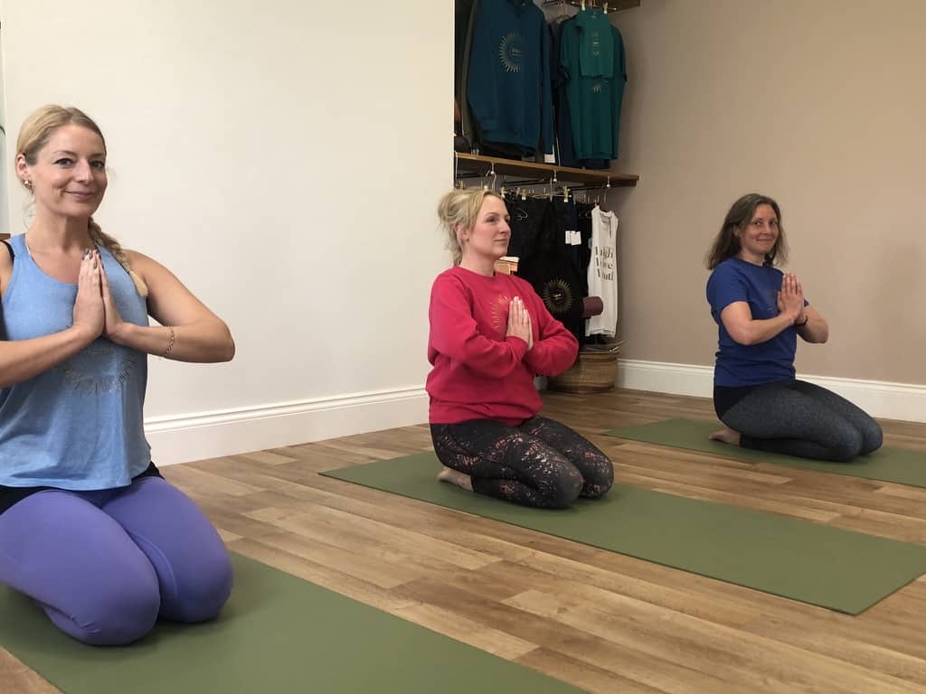 3 women sitting in namaste position in a yoga class at shine With Tabitha Yoga Studio in Belper Derbyshire